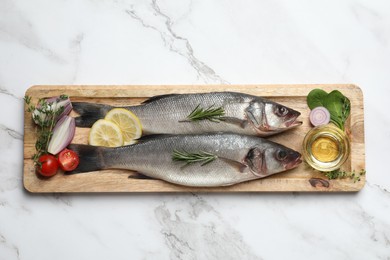Tasty sea bass fish and ingredients on white marble table, top view