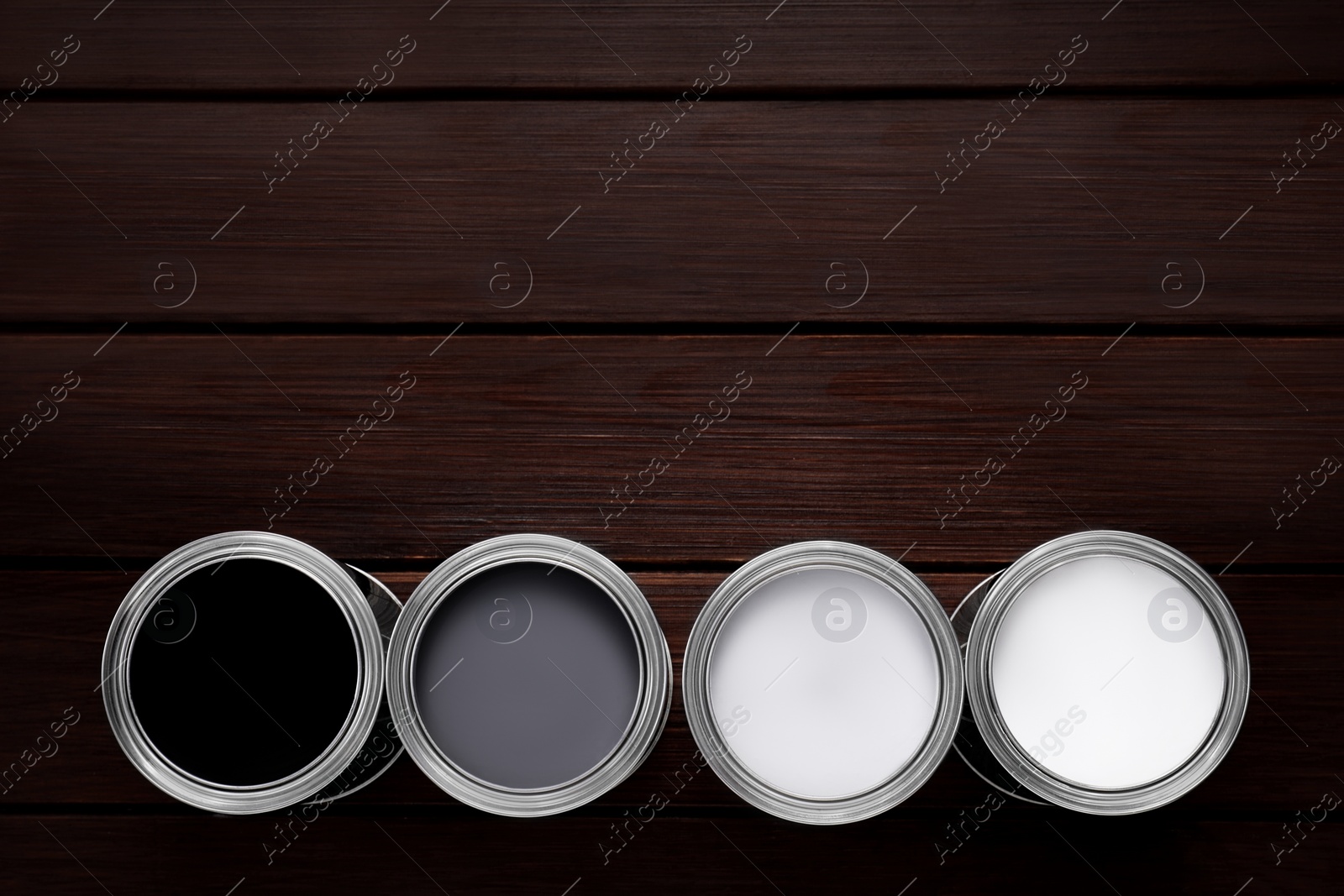 Photo of Cans of white, grey and black paints on wooden table, flat lay. Space for text