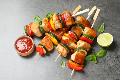 Delicious chicken shish kebabs with vegetables and ketchup on grey table