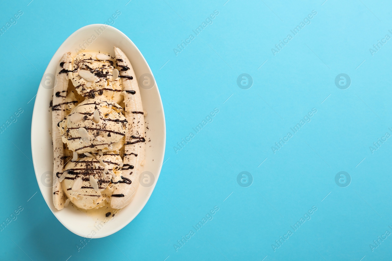 Photo of Delicious banana split ice cream with toppings on light blue background, top view. Space for text