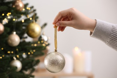 Photo of Woman holding shiny ball near Christmas tree indoors, closeup