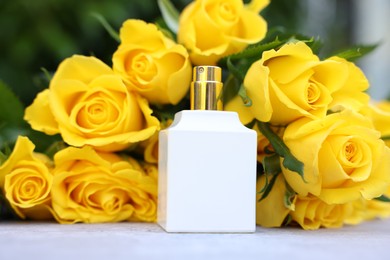 Perfume and beautiful bouquet of yellow roses on light table, closeup