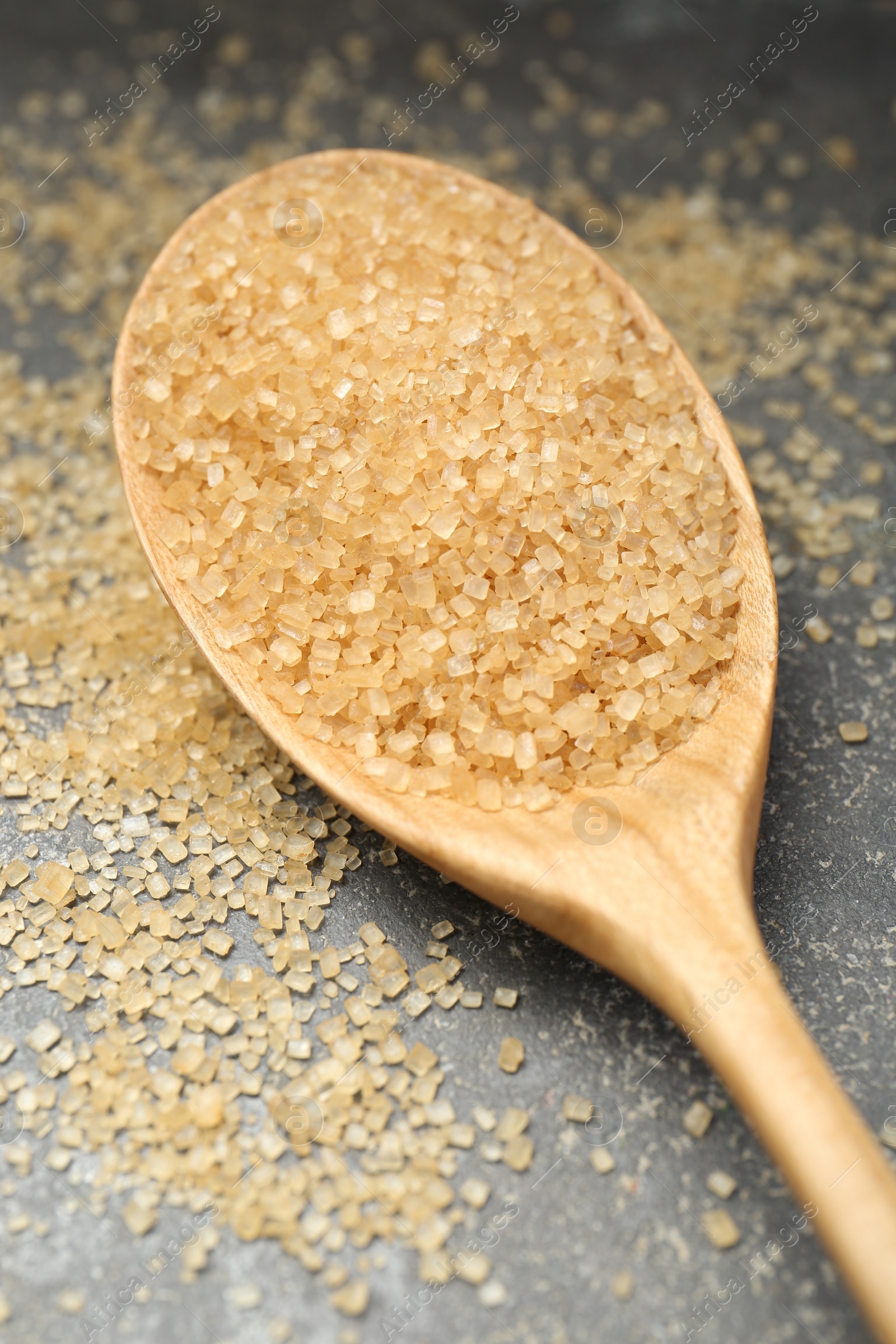 Photo of Spoon with brown sugar on grey textured table, closeup