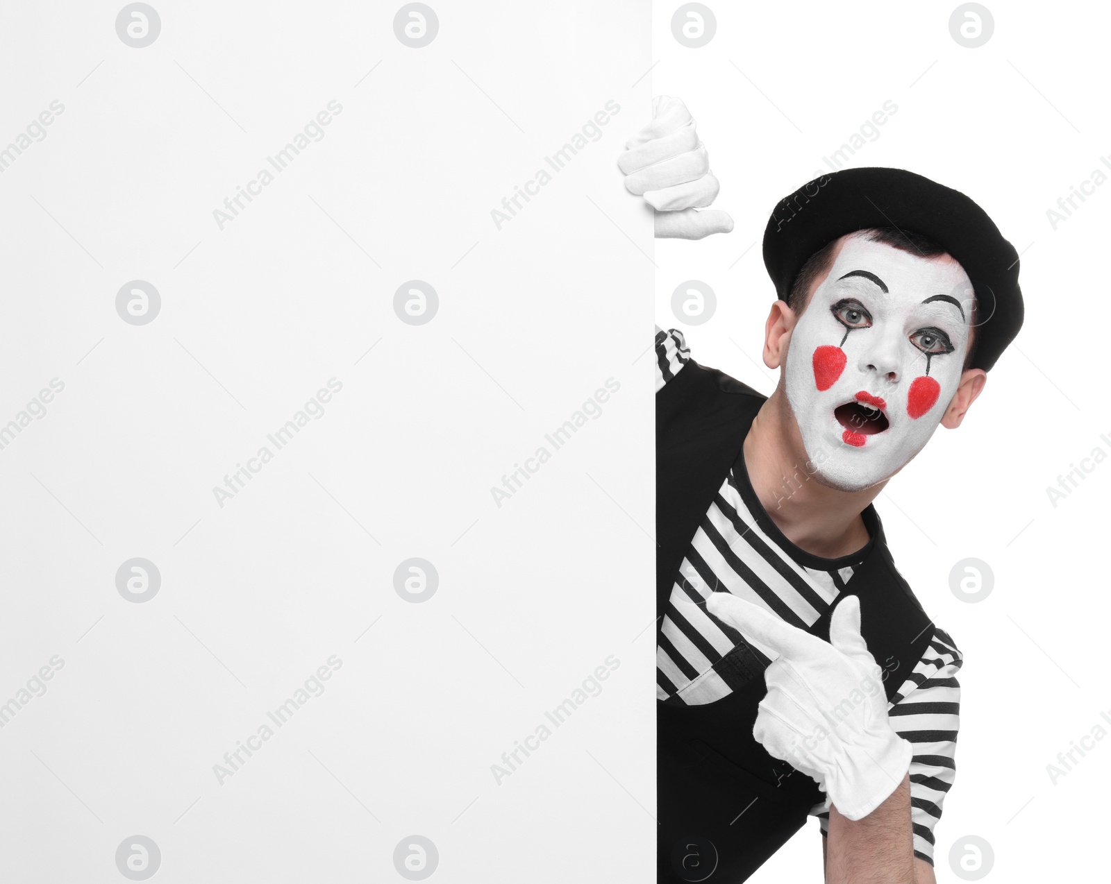 Photo of Funny mime artist peeking out of blank poster on white background