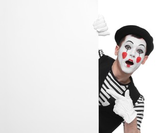 Funny mime artist peeking out of blank poster on white background