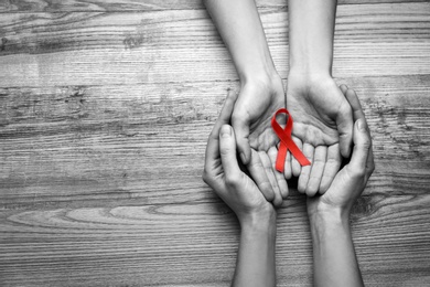 Image of World AIDS disease day. Women holding red awareness ribbon on wooden background, top view with space for text