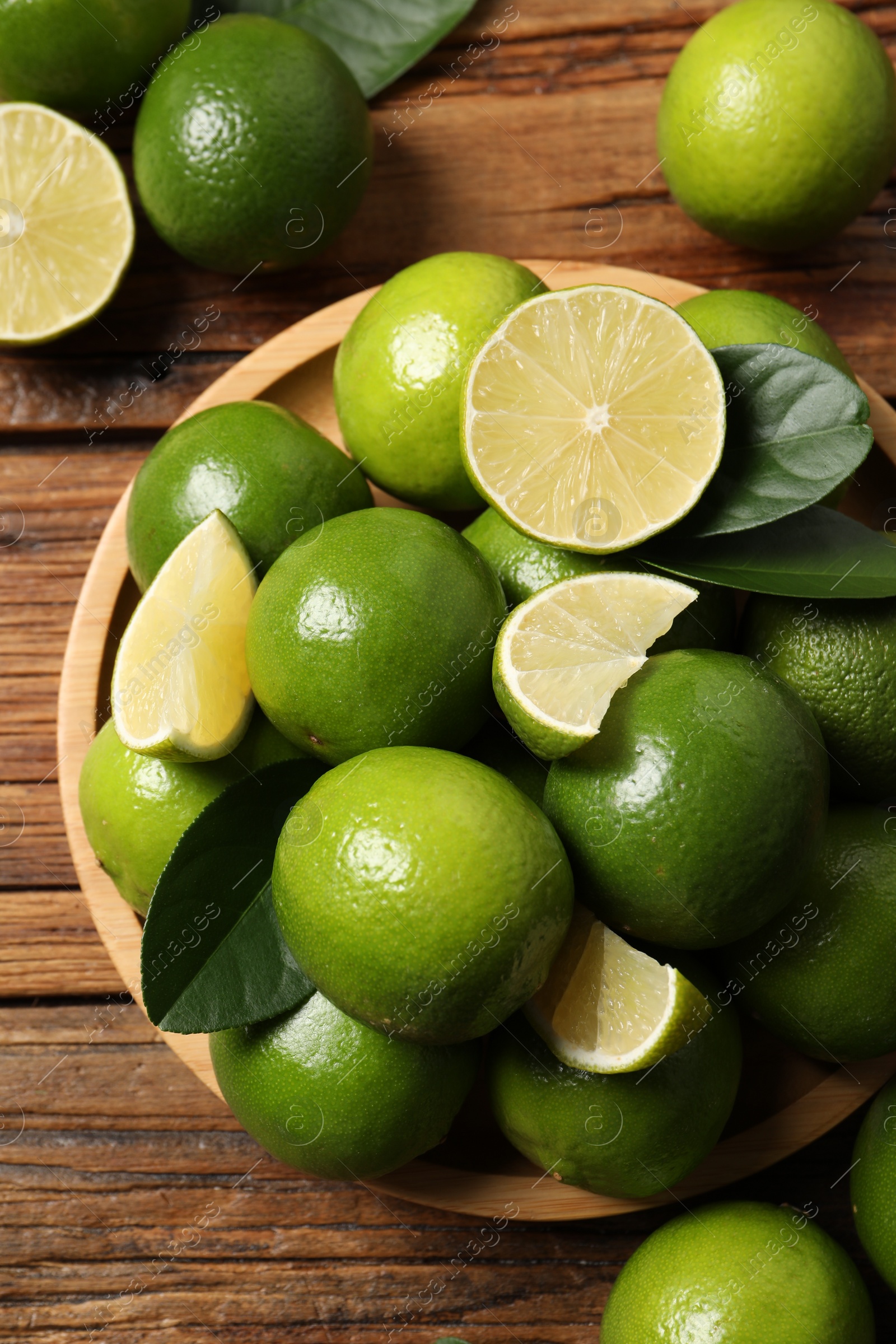 Photo of Fresh limes and green leaves on wooden table, top view