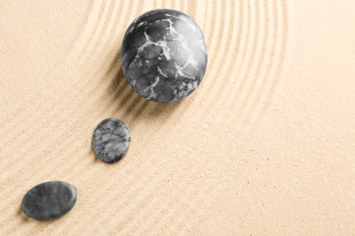 Photo of Zen garden stones on beige sand with pattern, flat lay. Space for text