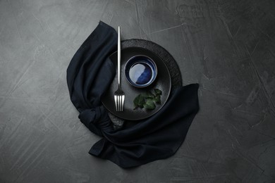 Photo of Stylish table setting. Dishes, fork, napkin and green leaves on grey surface, top view