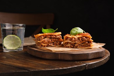 Photo of Delicious lasagna served on wooden table against black background