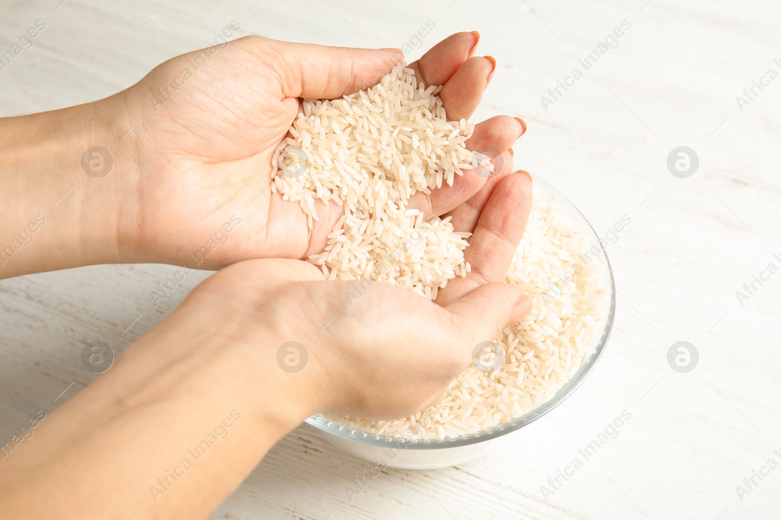 Photo of Woman holding uncooked rice over bowl at table, closeup