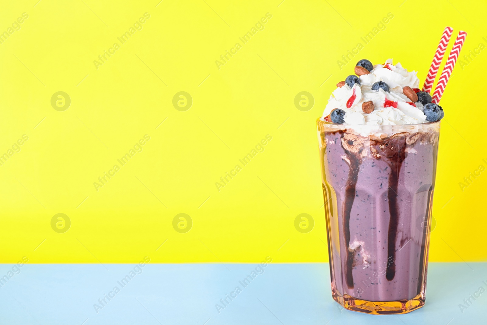 Photo of Tasty blueberry milk shake in glass on table against yellow background. Space for text