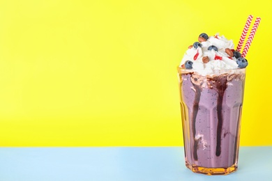 Photo of Tasty blueberry milk shake in glass on table against yellow background. Space for text