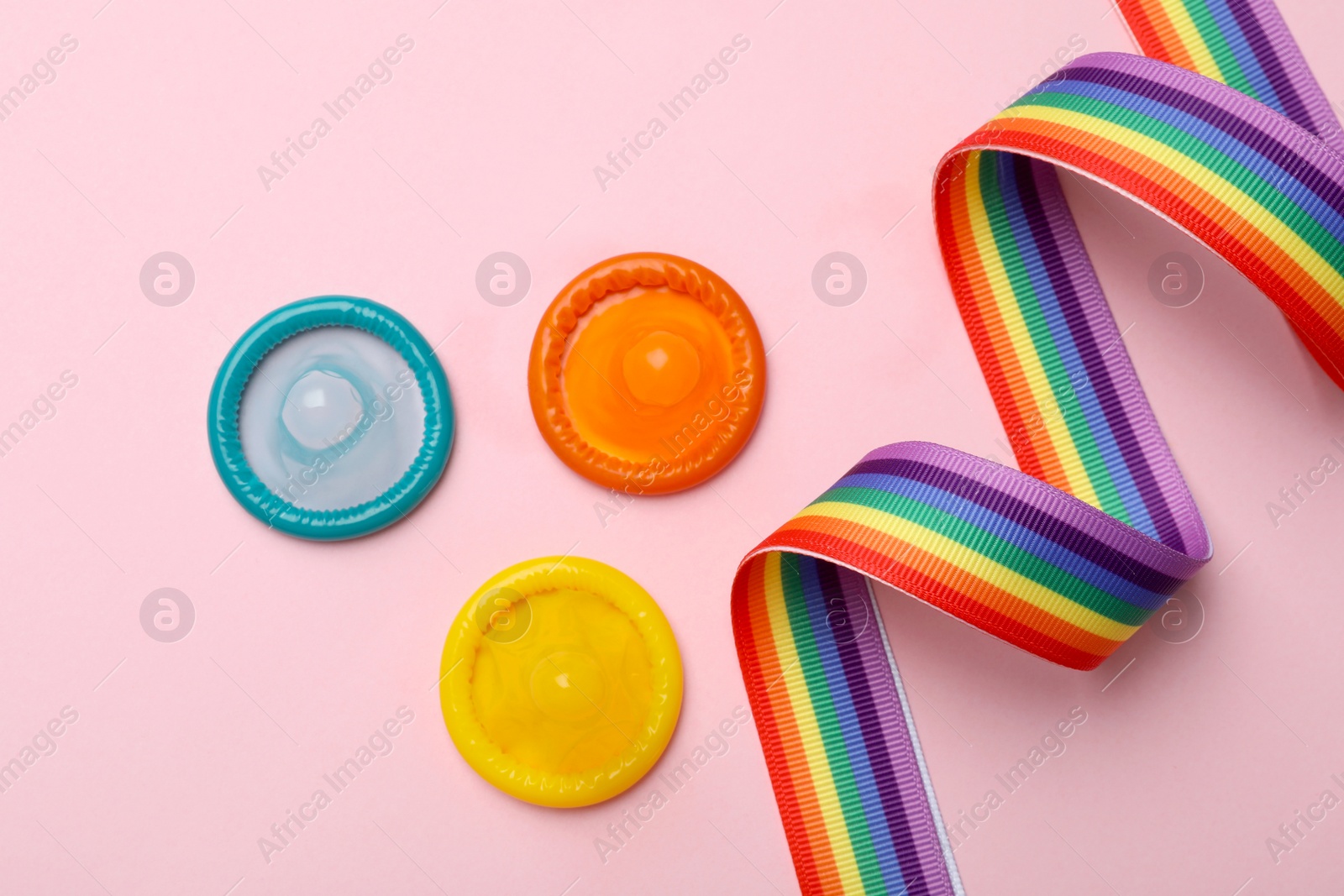 Photo of Flat lay composition with colorful condoms and rainbow ribbon on pink background. LGBT concept