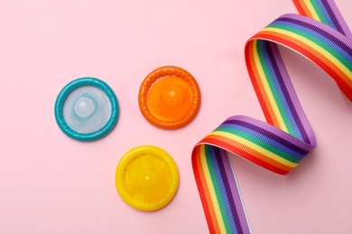 Flat lay composition with colorful condoms and rainbow ribbon on pink background. LGBT concept