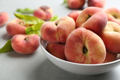 Photo of Fresh ripe donut peaches in bowl on light table, closeup
