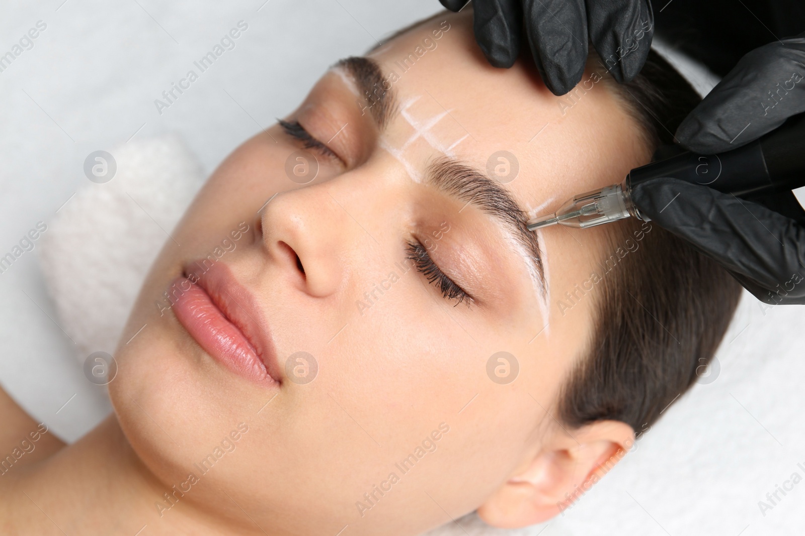 Photo of Beautician making permanent eyebrow makeup to young woman, closeup