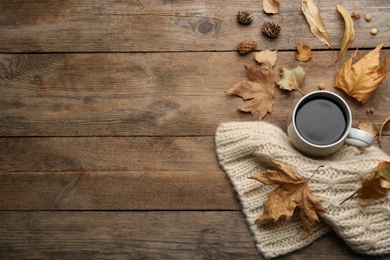 Flat lay composition with cup of hot drink and autumn leaves on wooden table, space for text. Cozy atmosphere