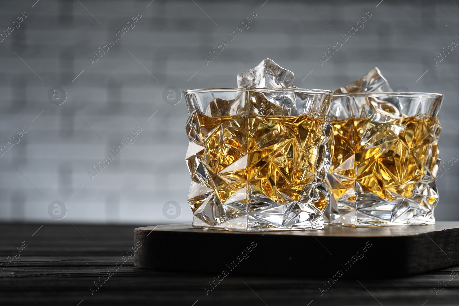 Photo of Whiskey and ice cubes in glasses on black wooden table, closeup. Space for text