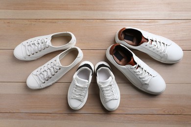 Photo of Set of new stylish white sneakers for entire family on wooden background, flat lay