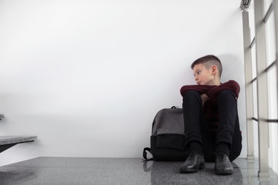 Photo of Upset boy with backpack sitting on staircase indoors. Space for text