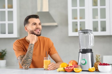 Handsome man with delicious smoothie at white marble table in kitchen