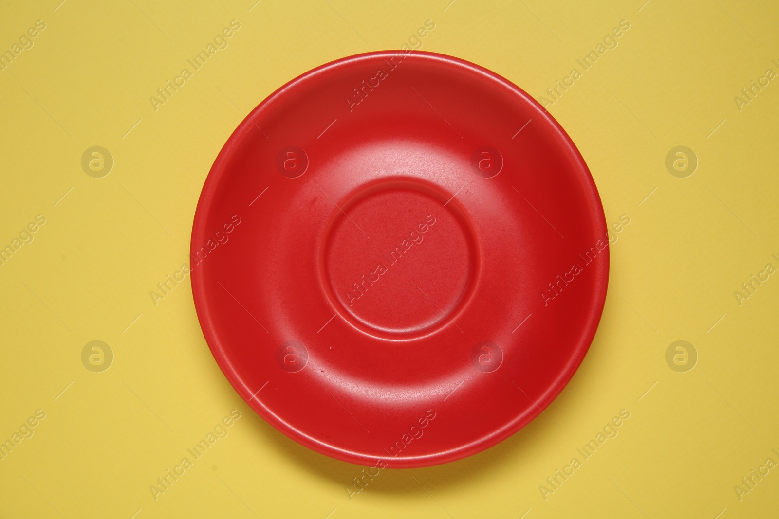 Photo of One red ceramic plate on yellow background, top view