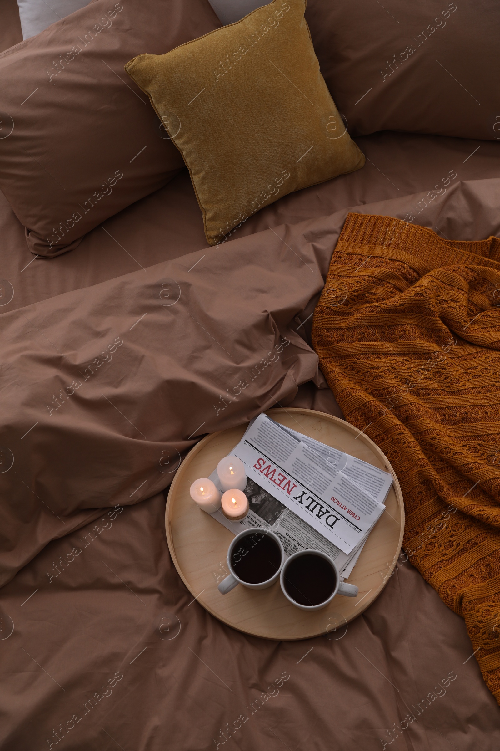 Photo of Cups of hot drink and candles on bed with brown linens, above view