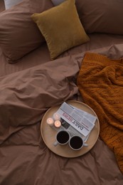 Photo of Cups of hot drink and candles on bed with brown linens, above view