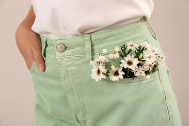Photo of Woman with beautiful tender flowers in pocket of jeans on light background, closeup