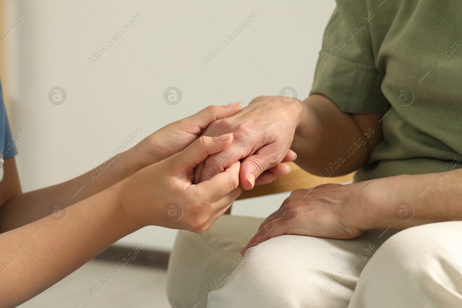 Photo of Young and elderly women holding hands indoors, closeup