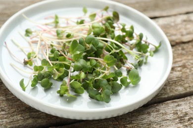 Photo of Plate with cut fresh radish microgreens on wooden table, closeup