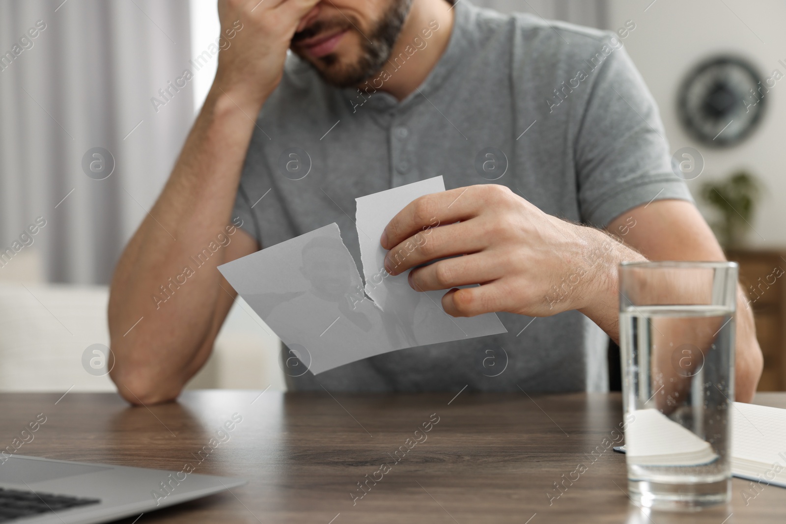 Photo of Man holding torn photo at table indoors, closeup. Divorce concept