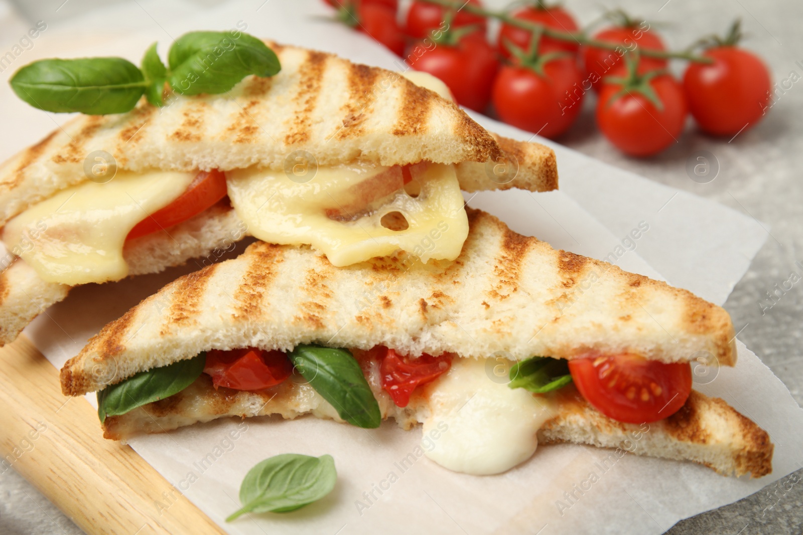 Photo of Delicious grilled sandwiches with mozzarella, tomatoes and basil on wooden board, closeup