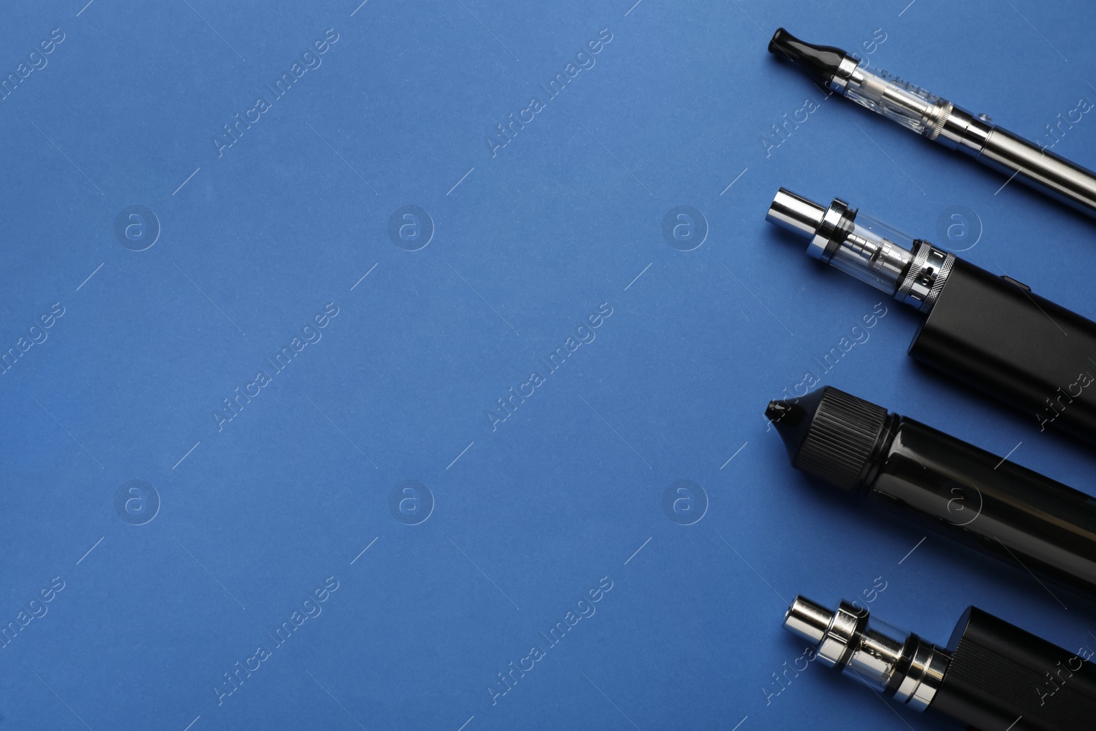 Photo of Many electronic smoking devices on blue background, flat lay. Space for text