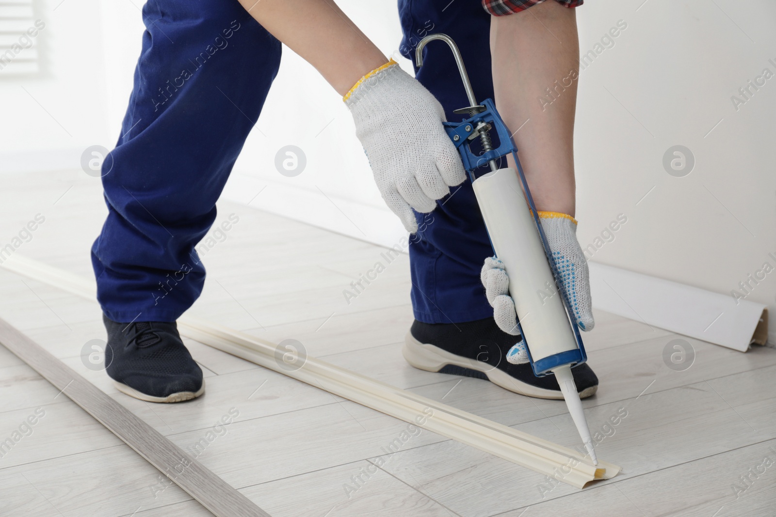 Photo of Man using caulking gun while installing plinth on laminated floor in room, closeup