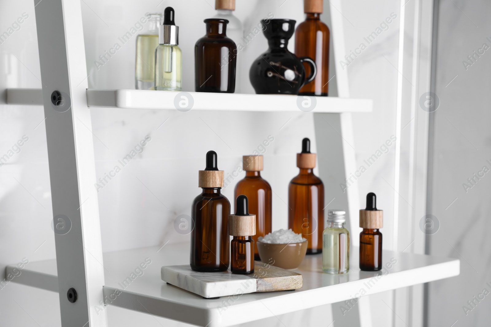 Photo of Essential oils, sea salt, and other cosmetic products on white shelving unit in bathroom