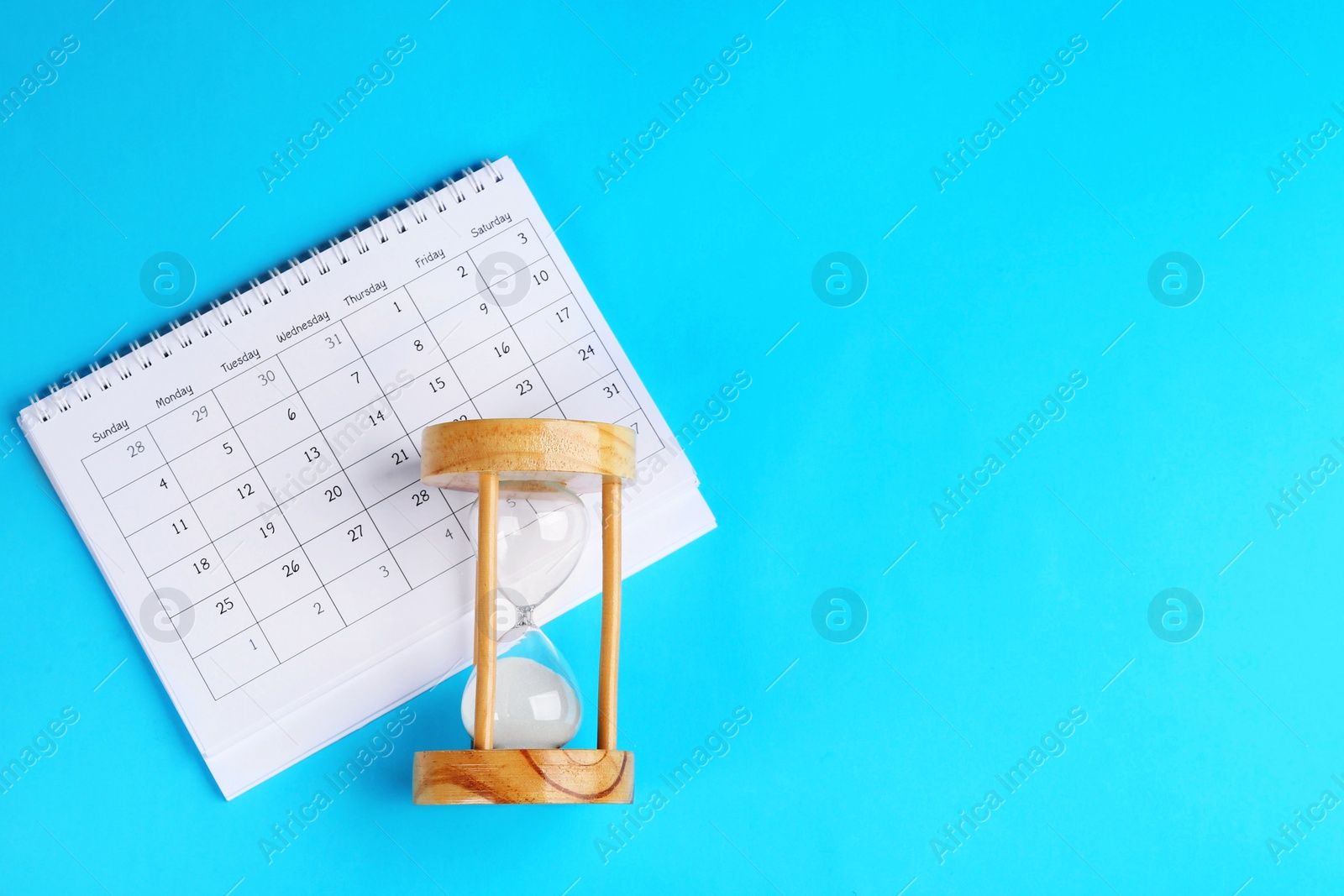 Photo of Calendar and hourglass on light blue background, flat lay. Space for text