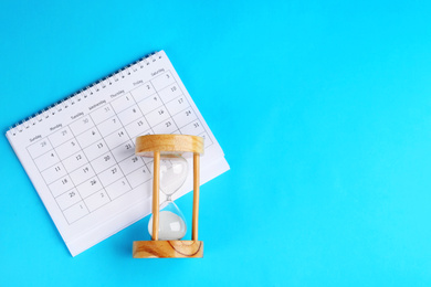 Photo of Calendar and hourglass on light blue background, flat lay. Space for text