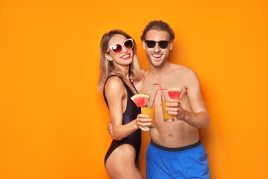 Happy young couple in beachwear with cocktails on color background