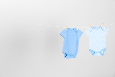 Different baby onesies hanging on clothes line against light grey background, space for text. Laundry day