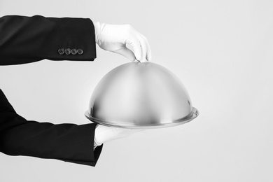 Photo of Waiter holding metal tray with lid on light background