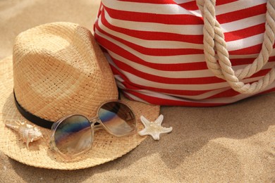 Stylish striped bag and beach accessories on sand, closeup