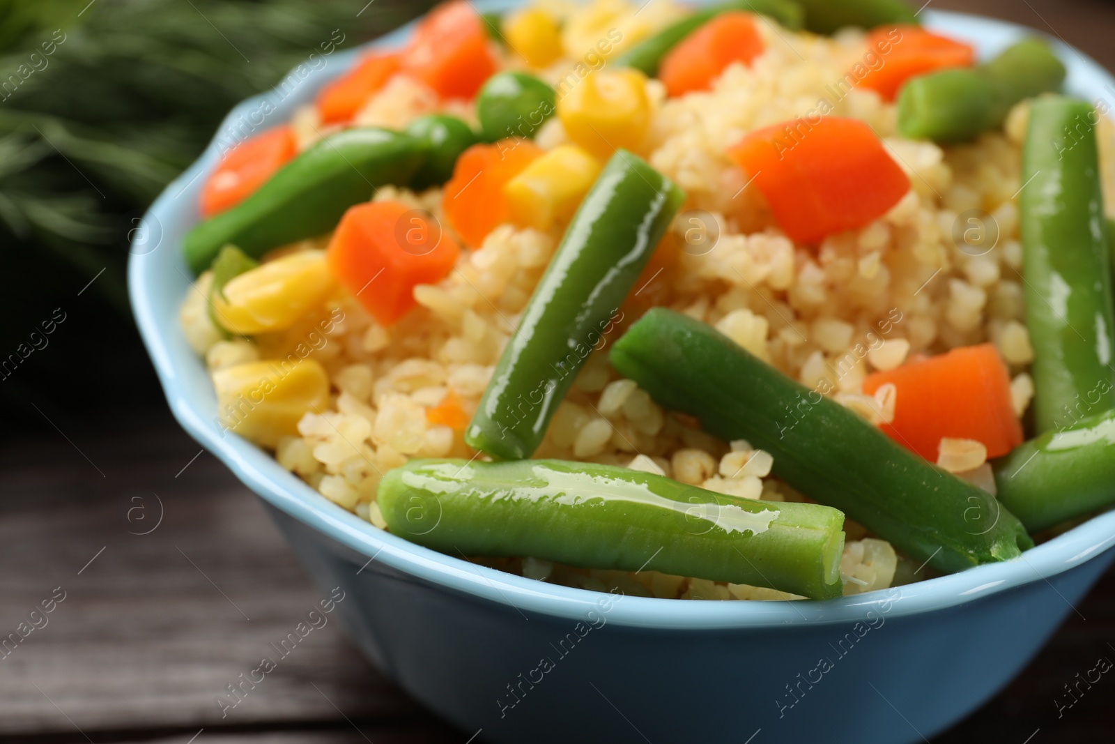 Photo of Delicious bulgur with vegetables in bowl on table, closeup