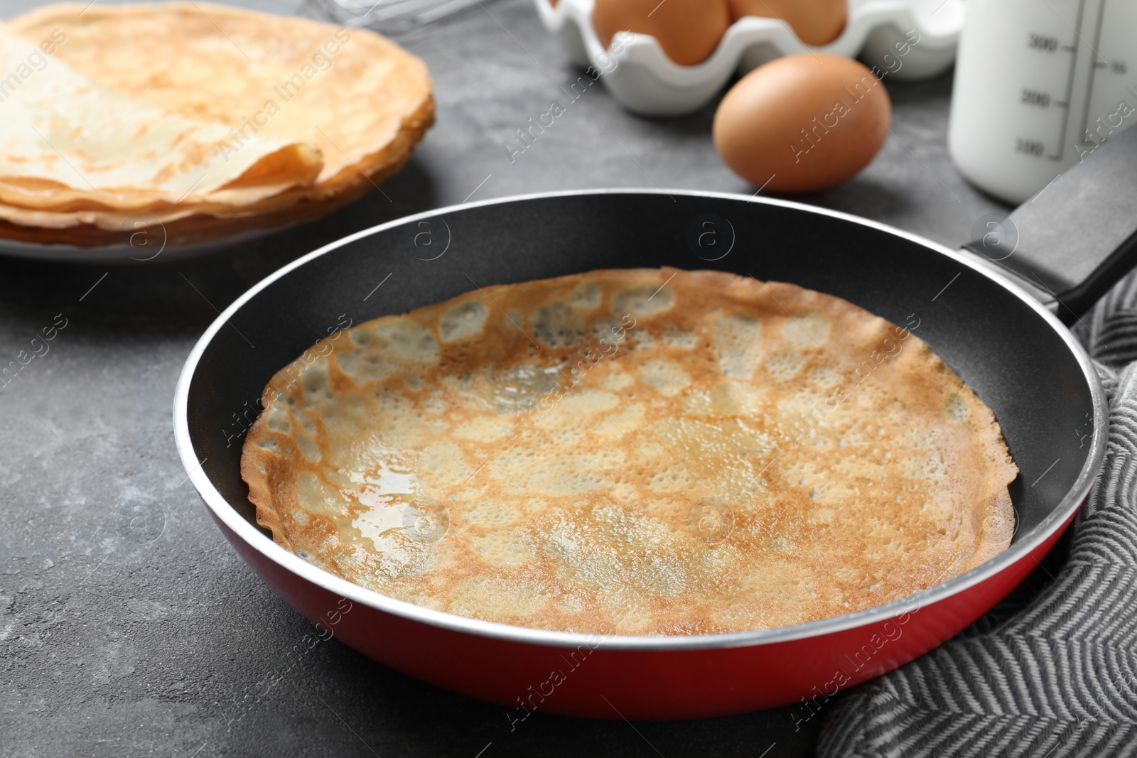 Photo of Delicious thin pancake in frying pan on grey table, closeup