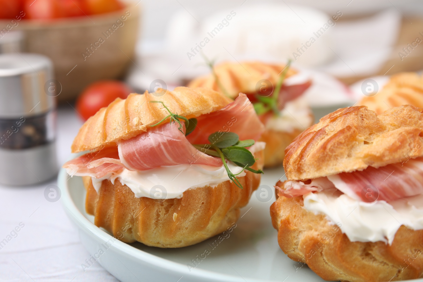 Photo of Delicious profiteroles with cream cheese and prosciutto on white table, closeup