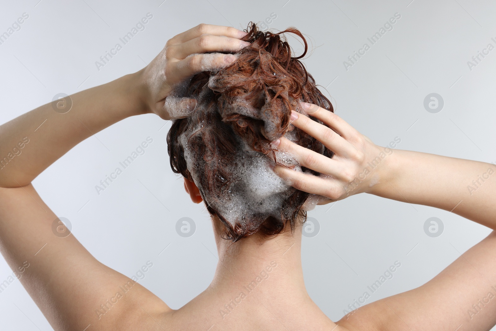 Photo of Young woman washing her hair with shampoo on light grey background, back view