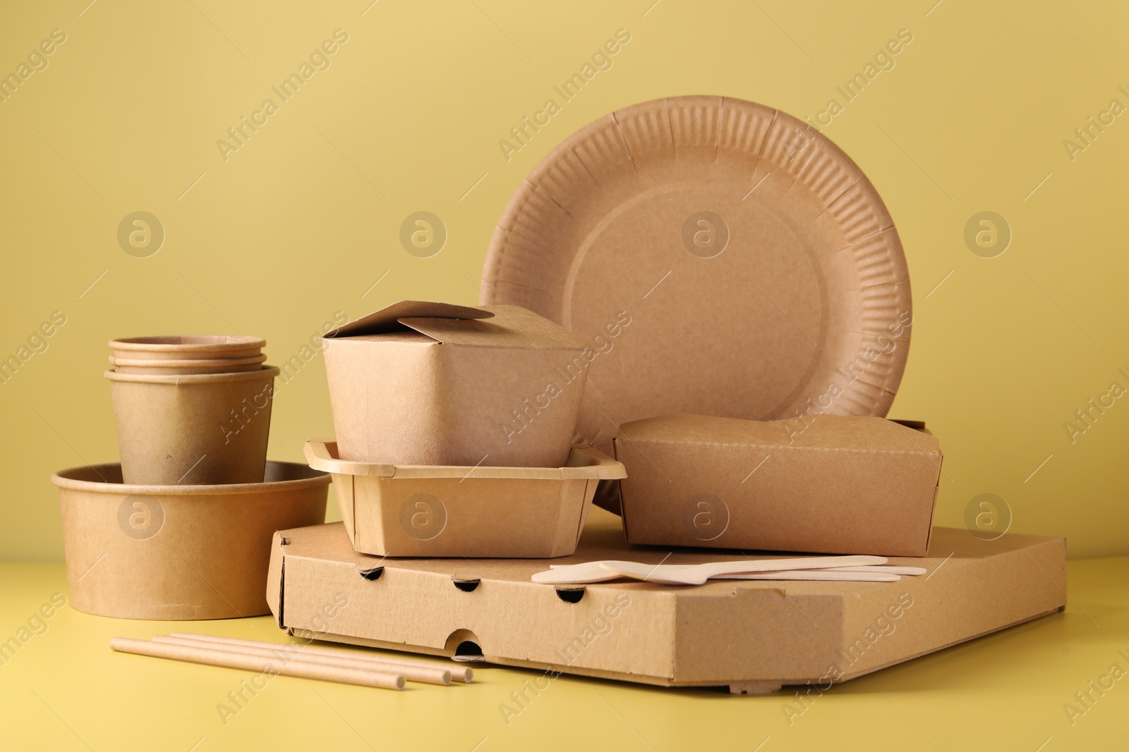 Photo of Eco friendly food packaging. Paper containers and tableware on pale yellow background