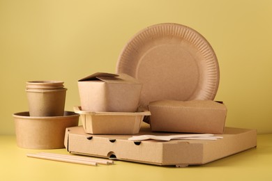 Photo of Eco friendly food packaging. Paper containers and tableware on pale yellow background