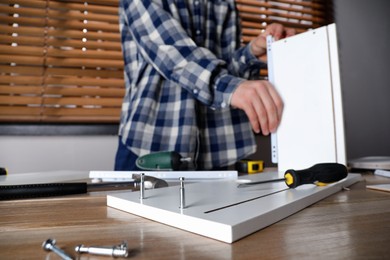 Photo of Man assembling furniture at table indoors, closeup. Selective focus